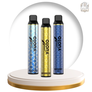 Three Yuoto disposable vape devices standing upright on a white and gold circular pedestal. The left device is light blue with a geometric pattern and labeled 'Blueberry Ice'; the center device is metallic gold with a geometric pattern and labeled 'Bananaice'; the right device is dark blue with a geometric pattern and labeled 'Blueberry Ice'.