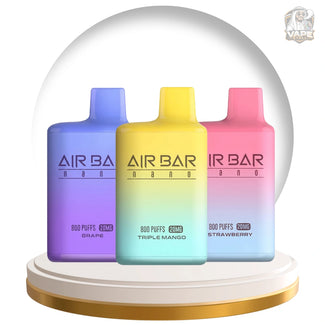 Three AIR BAR vape devices in a snow globe display: Grape purple, Triple Mango yellow-green, and Strawberry pink, on a white and gold base.