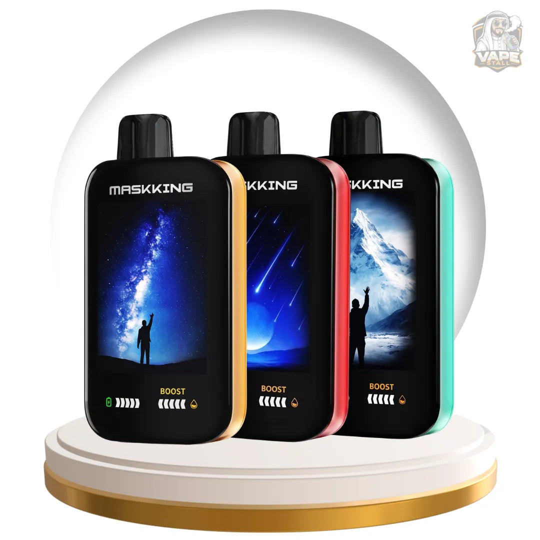Three MASKING Boost disposable vape devices in black, gold, red, and teal, displayed side-by-side on a white and gold circular pedestal. The vapes feature landscape-themed screens showing a starry night, shooting stars, and an icy mountain scene.
