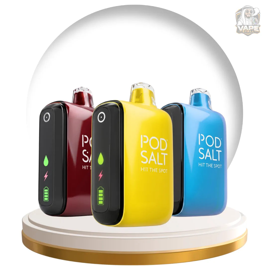 Four Pod Salt vape devices in black, burgundy, yellow, and blue, arranged on a white and gold circular pedestal inside a clear glass dome. The center yellow device is in front and displays the text 'POD SALT HIT THE HOT'.