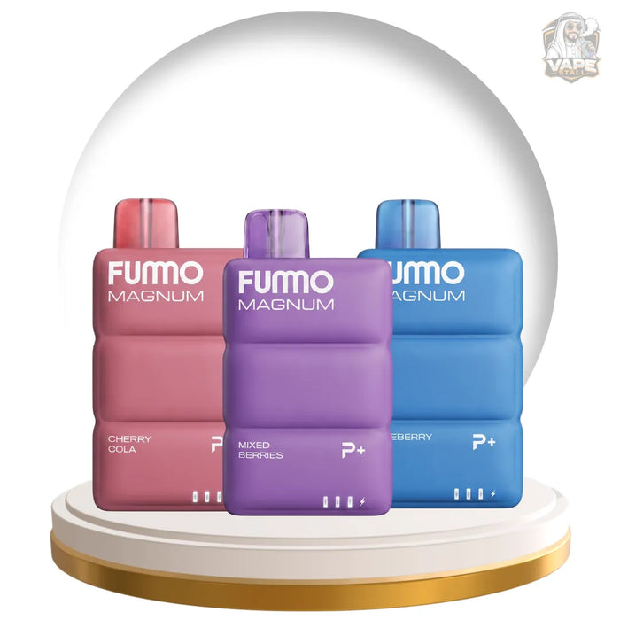 Three FUMO MAGNUM vape devices displayed side by side under a clear dome on a white and gold pedestal. The devices are in three different colors: a pinkish-red Cherry Cola flavor, a purple Mixed Berry flavor, and a blue Blueberry flavor.