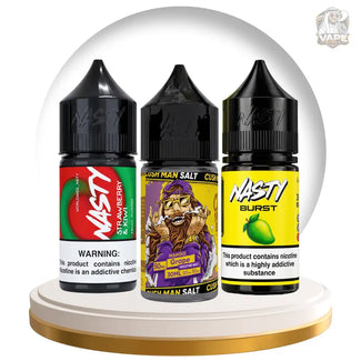 Three small NASTY e-liquid bottles displayed on a white and gold pedestal inside a clear dome. The bottles are black with colorful labels: Strawberry, Sour Grape, and Lemon Lime.